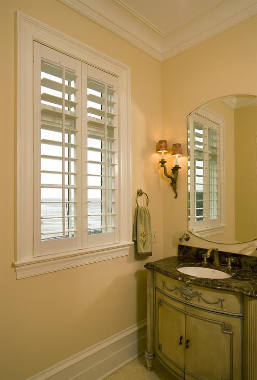 White plantation shutters in a light bathroom give a view of the ocean